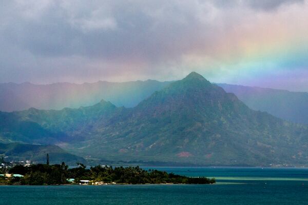 FILE -A rainbow is seen in the sky from President Barack Obama's motorcade as it passes Kaneohe Bay heading for the beach at Bellows Air Force Station, Saturday, Jan. 3, 2015, on the island of Oahu in Hawaii, on the final day of the Obama family vacation. (AP Photo/Jacquelyn Martin, File)