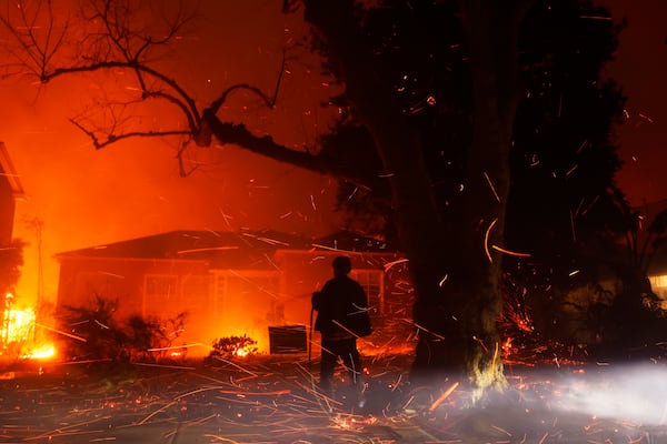 A person tries to hose down embers from the Palisades Fire in the Pacific Palisades neighborhood of Los Angeles, Tuesday, Jan. 7, 2025. (AP Photo/Etienne Laurent)