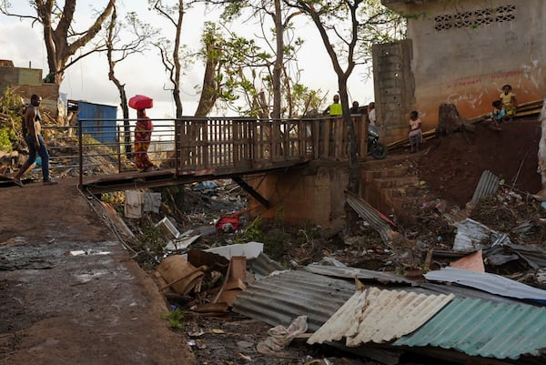 People walk past debris in the Kaweni slum Thursday, Dec. 19, 2024, on the outskirts of Mamoudzou, in the French Indian Ocean island of Mayotte, after Cyclone Chido. (AP Photo/Adrienne Surprenant)