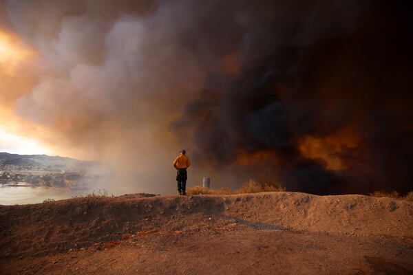 A firefighter looking out towards Lake Castaic stands on a mound backdropped by clouds of smoke caused by the Hughes Fire in Castaic, Calf., Wednesday, Jan. 22, 2025. (AP Photo/Ethan Swope)