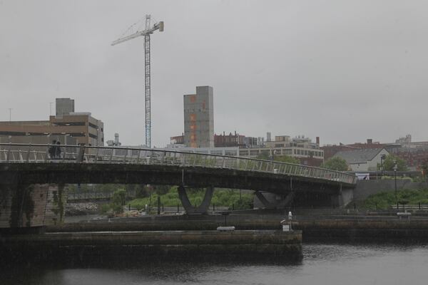 A man walks in the rain across a pedestrian bridge in Providence, R.I. on Thursday, May 22, 2025. (AP Photo/Kimberlee Kruesi)