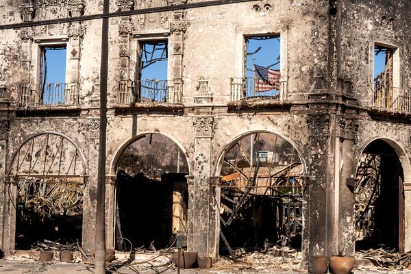 An American flag hangs behind a commercial building destroyed by the Palisades Fire in the Pacific Palisades neighborhood of Los Angeles, Sunday, Jan. 12, 2025. (AP Photo/Noah Berger)