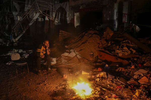 A man sits by a fire in an area littered with rubble from buildings demolished during the Israeli army's ground and air offensive against Hamas in Gaza City, Tuesday Feb. 4, 2025.(AP Photo/Abdel Kareem Hana)