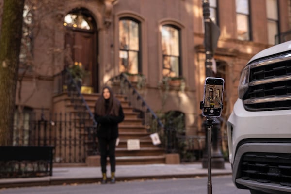 A phone is secured to a selfie stick as a person poses for a photo backdropped by the brownstone where Carrie Bradshaw lived in “Sex and the City”, in New York, Wednesday, Jan. 15, 2025. The city’s Landmarks Preservation Commission approved an application for a metal gate for the front staircase of the Manhattan brownstone to keep away tourists who endlessly trespass and pose for pictures. (AP Photo/Yuki Iwamura)