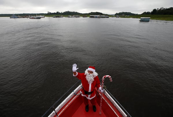 Jorge Barroso, dressed as Santa Claus, waves as he arrives on a boat to distribute Christmas gifts to children who live in the riverside communities of the Amazon, in Iranduba, Brazil, Saturday, Dec. 21, 2024. (AP Photo/Edmar Barros)