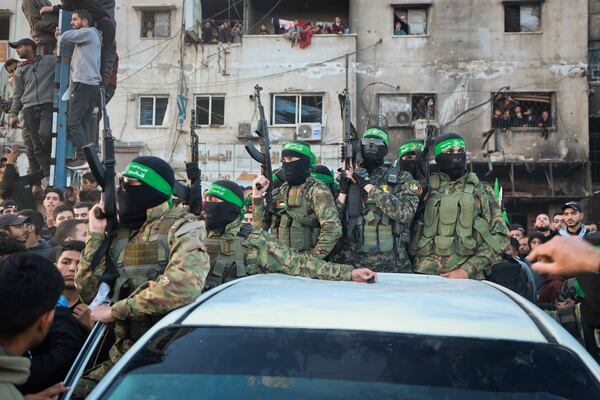 Fighters from the Qassam Brigades, the military wing of Hamas, stand atop a car as Red Cross vehicles maneuver to collect Israeli hostages released under a ceasefire agreement between Israel and Hamas, in Gaza City, Sunday, Jan. 19, 2025. (AP Photo/Abed Hajjar)