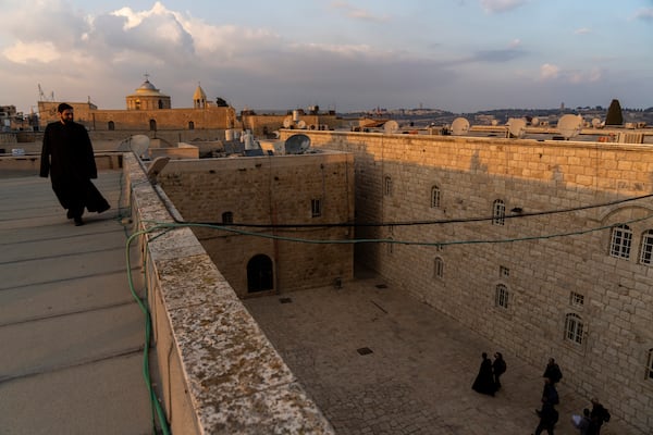 An Armenian Christian deacon walks on a roof terrace near St. James Cathedral, background, at the Armenian quarter in Jerusalem, Thursday, Nov. 21, 2024. (AP Photo/Francisco Seco)