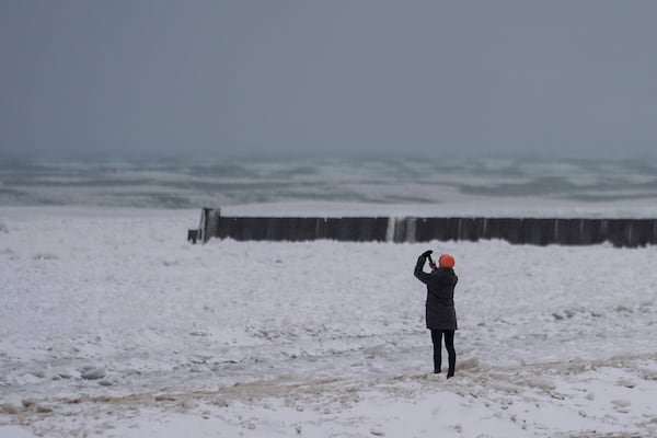 A person takes pictures as they walk on a beach along the shore of Lake Michigan, Wednesday, Feb. 12, 2025, in Chicago. (AP Photo/Kiichiro Sato)