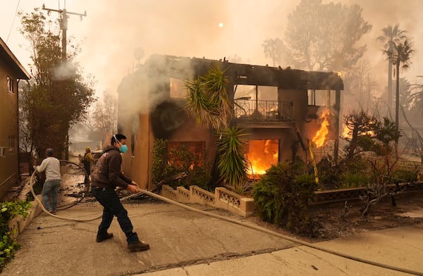 Pedestrians help a firefighter stretch a hose as an apartment building burns, Wednesday, Jan. 8, 2025, in the Altadena section of Pasadena, Calif. (AP Photo/Chris Pizzello)