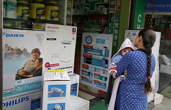 FILE- A woman carries an infant outside a shop selling air purifiers at a market place in New Delhi, India, on Nov. 14, 2017. (AP Photo/Altaf Qadri, File)