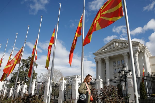 A woman walks past North Macedonia flags flapping in the wind at half staff in front of a Government building in Skopje, North Macedonia, Monday, March 17, 2025, following a massive fire in the nightclub in the town of Kocani, early Sunday. (AP Photo/Boris Grdanoski)