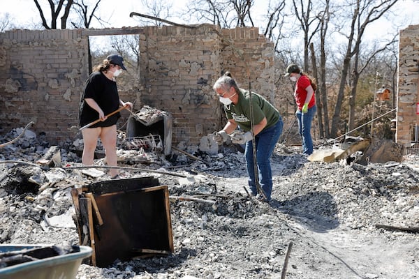 Friends and students of home owner Andrine Shufran, look through the ashes that are left of her home in the Hidden Oaks neighborhood in Stillwater, Okla. on Monday, March 17, 2025 after wildfires burned through the area Friday. (AP Photo/Alonzo Adams)