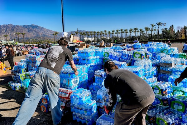 Volunteers stack donated water for people impacted by the Altadena Fire at a donation center at Santa Anita Park in Arcadia, Calif., on Wednesday, Jan. 15, 2025. (AP Photo/Richard Vogel)