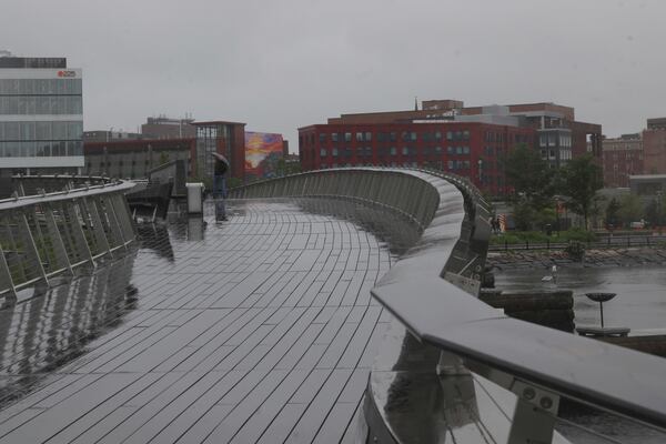A man walks in the rain across a pedestrian bridge in Providence, R.I. (AP Photo/Kimberlee Kruesi)