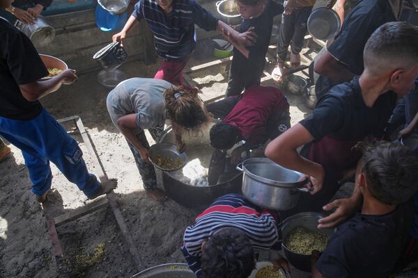 Palestinian children scrape a pot for leftover food after all meals were distributed at a community kitchen in Khan Younis, southern Gaza Strip, on Friday, May 9, 2025.
