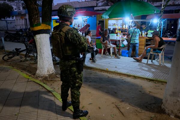 Residents gather under the watch of a soldier in Tibu, Colombia, on Monday, Jan. 20, 2025, following a series of guerrilla attacks that have killed dozens and forced thousands to flee their homes in the Catatumbo region. (AP Photo/Fernando Vergara)