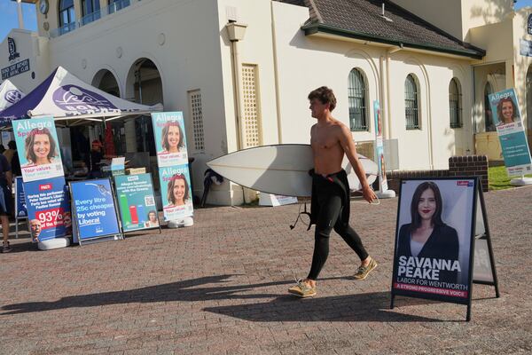A surfer carries his board as he walks past a polling booth at Sydney's Bondi Beach, Saturday, May 3, 2025. (AP Photo/Mark Baker)