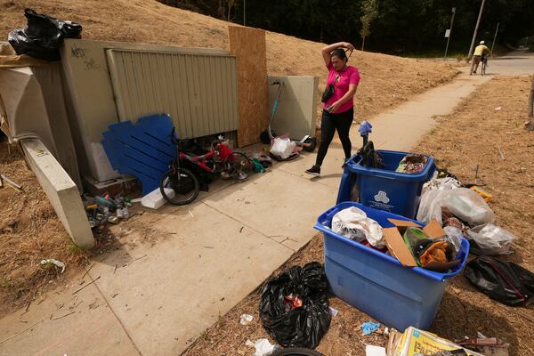 A pedestrian walks past trash left outside a bin near a homeless encampment, Monday, May 12, 2025, in Los Angeles. (AP Photo/Damian Dovarganes)