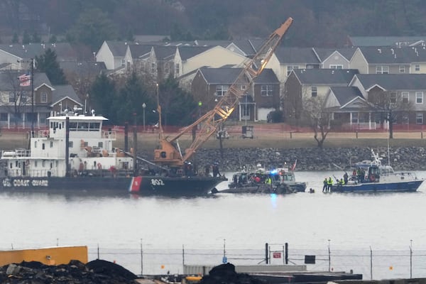 A member of a dive team and a Coast Guard vessel with a crane are pictured as they work near the wreckage of a Black Hawk helicopter in the Potomac River from Ronald Reagan Washington National Airport, Friday, Jan. 31, 2025, in Arlington, Va. (AP Photo/Alex Brandon)