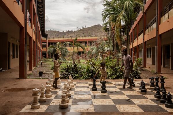 People interact by an outdoor chess board, after finding refuge at the Lycée des Lumières after losing their homes, in Mamoudzou, Mayotte, Thursday, Dec. 19, 2024. (AP Photo/Adrienne Surprenant)