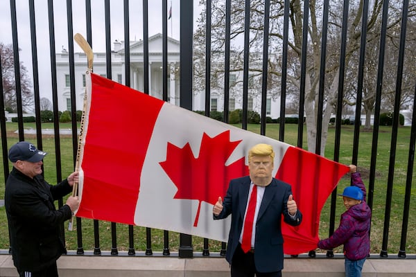 Toronto residents Douglas Bloomfield, from right, and his son Phoenix, who are on vacation in Washington, hold a Canadian flag and an ice hockey stick to show their support for Canada regarding trade tariffs as they pose with with another visitor to the city wearing a mask of President Donald Trump in front of the White House in Washington, Thursday, March 13, 2025. (AP Photo/Ben Curtis)