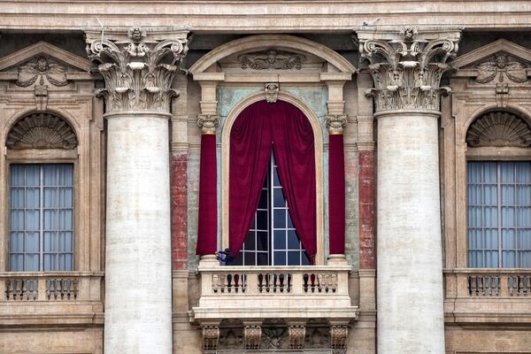 A man gives the last touch to a red drape wrapped around a column of the central lodge of St. Peter's Basilica in Vatican City, Monday, May 5, 2025, before the conclave starting on May 7, where they will elect the 267th pontiff of the Catholic Church. (AP Photo/Gregorio Borgia)