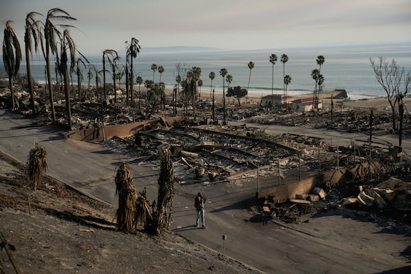 A person walks past damage from the Palisades Fire on Friday, Jan. 10, 2025, in the Pacific Palisades section of Los Angeles. (AP Photo/John Locher)