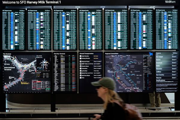 A traveler walks past screens showing outgoing and incoming flights at San Francisco International Airport ahead of the Memorial Day holiday weekend in San Francisco, Thursday, May 22, 2025. (AP Photo/Godofredo A. Vásquez)