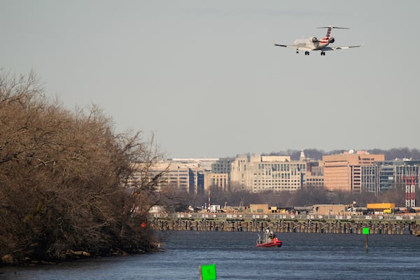 A Coast Guard boat works in the Potomac river as an American Airlines jet approaches Ronald Reagan Washington National Airport Saturday, Feb. 1, 2025, in Arlington, Va., near the wreckage site where an American Airlines jet and a Black Hawk helicopter collided, as seen from Alexandria, Va. (AP Photo/Carolyn Kaster)