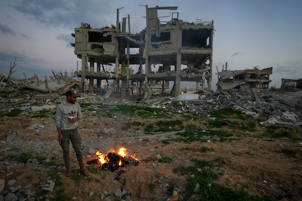 A man stands by a fire next to a destroyed house in an area littered with rubble from buildings demolished during the Israeli army's ground and air offensive against Hamas in Gaza City, Tuesday Feb. 4, 2025.(AP Photo/Abdel Kareem Hana)