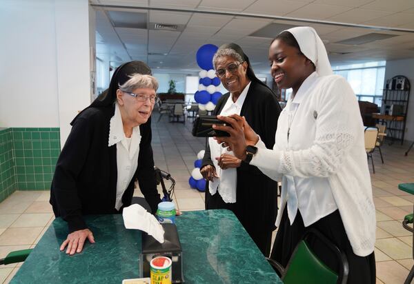 Sr. Ann Elise Sonnier, left, and Sister Clara Mae Jackson, center, look at photos on Sister Seyram Mary Adzokpa's phone at the Sisters of the Holy Family in New Orleans, Wednesday, June 26, 2024. (AP Photo/Jessie Wardarski)