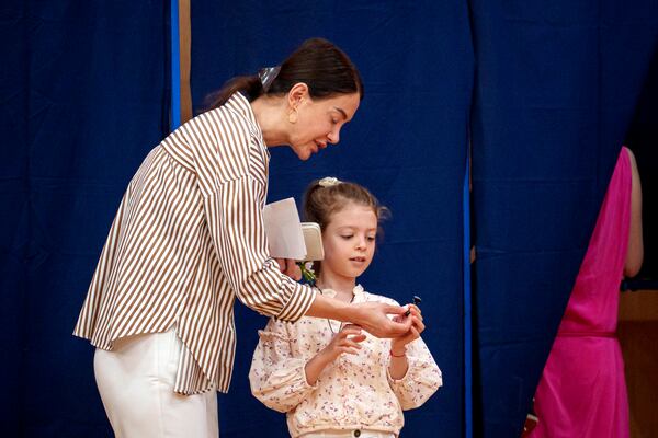 A woman hands a little girl a voting stamp after exiting a voting booth before casting her vote in the first round of the presidential election redo in Bucharest, Romania, Sunday, May 4, 2025. (AP Photo/Andreea Alexandru)