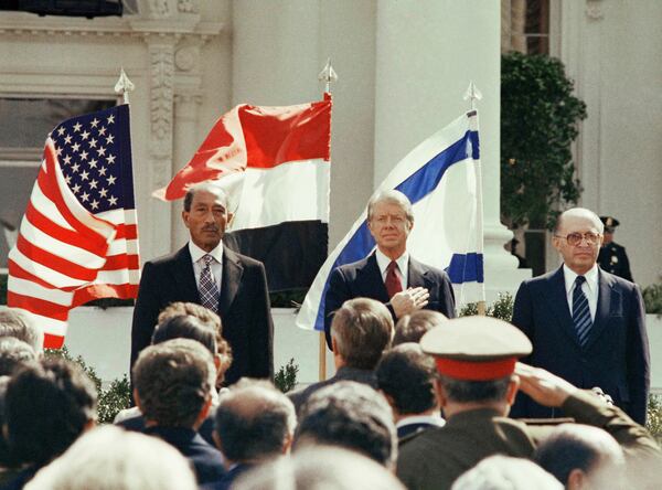 FILE - President Jimmy Carter stands in front of the billowing flags of Egypt, on the left, and Israel as the national anthems of the three countries are played before the signing of the peace treaty at the White House in Washington, March 26, 1979. (AP Photo, File)