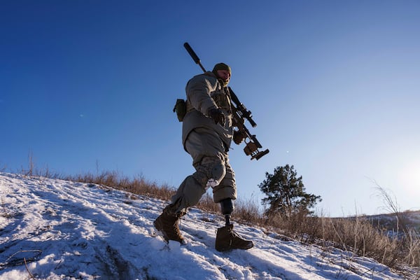 Serhii Pozniak, a commander with a Ukrainian sniper unit who lost a leg after stepping on a mine, carries his rifle during training near Kyiv, Ukraine on Feb. 17, 2025. (AP Photo/Evgeniy Maloletka)