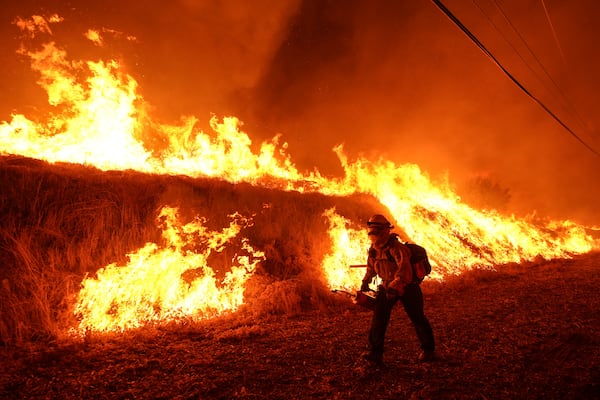 A firefighter carries a drip torch as he ignites a backfire against the Hughes Fire burning along a hillside in Castaic, Calif., Wednesday, Jan. 22, 2025. (AP Photo/Jae C. Hong)