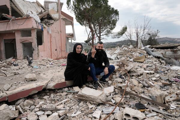 Lebanese citizens flash victory signs, as they sit on the rubble of a destroyed house caused by the Israeli air and ground offensive, in Aita al-Shaab, a Lebanese border village with Israel, south Lebanon, Sunday, Jan. 26, 2025. (AP Photo/Bilal Hussein)