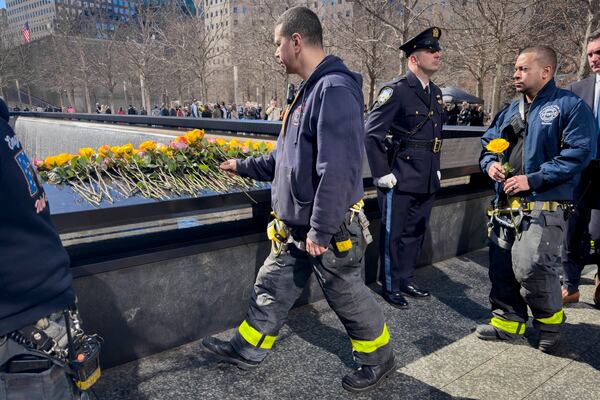 A firefighter places a flower on the names of the deceased during a ceremony marking the anniversary of the 1993 World Trade Center bombing at the 9/11 Memorial, Wednesday, Feb. 26, 2025, in New York. (AP Photo/John Minchillo)