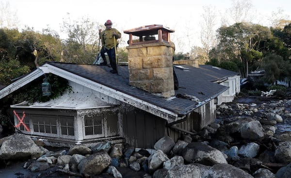 FILE - A firefighter stands on the roof of a house submerged in mud and rocks, Jan. 10, 2018, in Montecito, Calif. (AP Photo/Marcio Jose Sanchez, File)