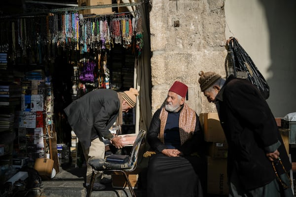 A man sits next to a vendor setting up his shop in the Old City , near the Umayyad Mosque, ahead of Friday prayers in Damascus, Syria, Friday, Dec. 20, 2024. (AP Photo/Leo Correa)