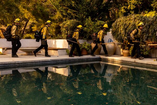 A Cal Fire hand crew walks past a swimming pool toward their next assignment during the Palisades Fire in the Mandeville Canyon neighborhood of Los Angeles, Calif., Saturday, Jan. 11, 2025. (Stephen Lam/San Francisco Chronicle via AP)