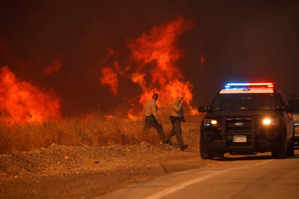 County Sheriff officers return to their vehicle after monitoring flames caused by the Hughes Fire along a roadside in Castaic, Calf., Wednesday, Jan. 22, 2025. (AP Photo/Ethan Swope)