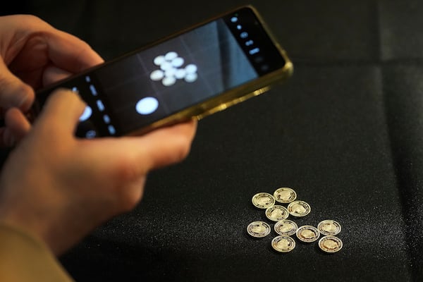 A visitor takkes a picture of small coins on her phones during the "Trial of the Pyx,'' a ceremony that dates to the 12th Century in which coins are weighed in order to make certain they are up to standard, at the Goldsmiths' Hall in London, Tuesday, Feb. 11, 2025.(AP Photo/Frank Augstein)