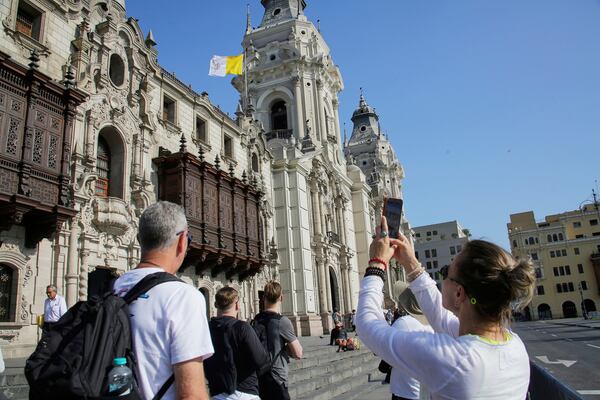 A woman photographs the Vatican flag flying above the Cathedral in Lima, Peru, following the election of Robert Prevost, a dual citizen of the United States and Peru who served as a missionary and bishop in the country, as Pope Leo XIV, Thursday, May 8, 2025. (AP Photo/Cesar Zamalloa)