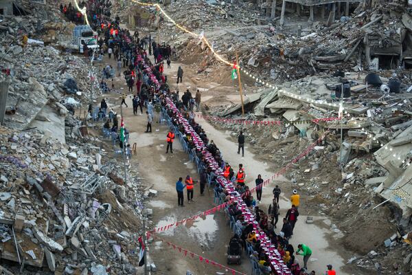 Palestinians sit at a large table surrounded by the rubble of destroyed homes and buildings as they gather for iftar, the fast-breaking meal, on the first day of Ramadan in Rafah, southern Gaza Strip, Saturday, March 1, 2025 (AP Photo/Abdel Kareem Hana)