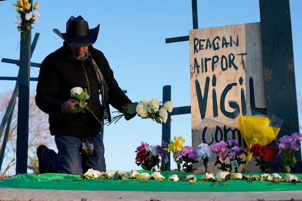 Roberto Marquez, of Dallas, places flowers at a memorial for the 67 victims of a midair collision between an Army helicopter and an American Airlines flight from Kansas near the Ronald Reagan Washington National Airport, Saturday, Feb. 1, 2025, in Arlington, Va. (AP Photo/Carolyn Kaster)