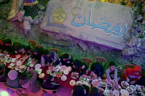 Palestinians hold a collective suhoor meal next to their destroyed homes for the holy month of Ramadan in Khan Younis, southern Gaza Strip, Friday, Feb. 28, 2025. Arabic reads: "Ramadan." (AP Photo/Jehad Alshrafi)