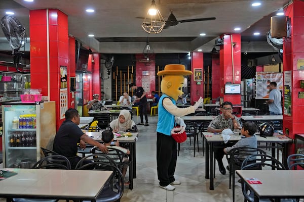 A street busker gestures as he talks to a guests at a coffee shop in Banda Aceh, Indonesia, Friday, Dec. 13, 2024. (AP Photo/Achmad Ibrahim)