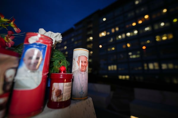 Candles with pictures of Pope Francis are laid under the statue of late Pope John Paul II outside Agostino Gemelli Polyclinic in Rome, Wednesday, Feb. 19, 2025, where the Pontiff is hospitalized since Friday, Feb. 14. (AP Photo/Andrew Medichini)