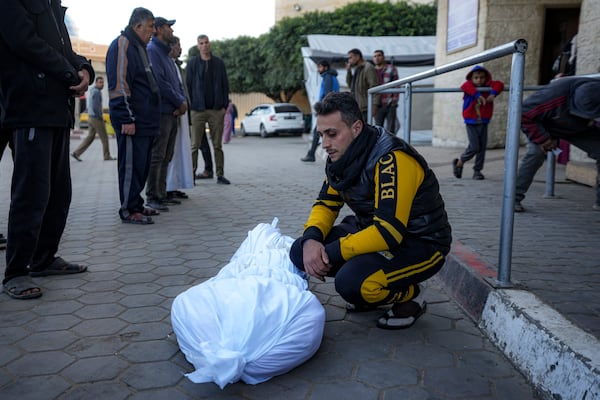 A man sits by the body of a Palestinian killed in the Israeli bombardment of the Gaza Strip at Al-Aqsa Hospital in Deir Al-Balah, Wednesday, Dec. 25, 2024. (AP Photo/Abdel Kareem Hana)