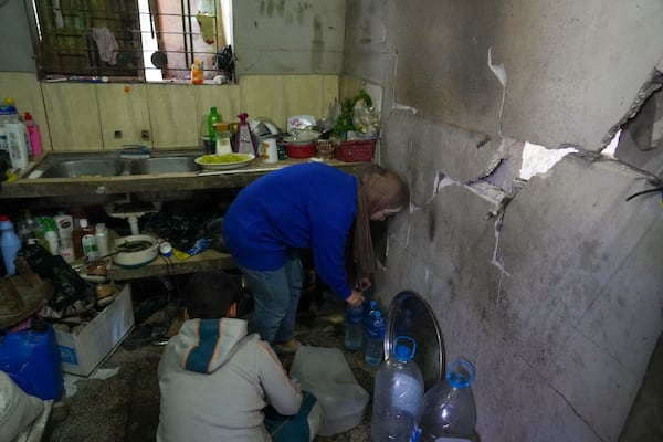 Rawya Tamboura and her son Yazan fill bottles with water inside their home, which was struck by an Israeli airstrike on Oct. 20, 2023, in Beit Lahiya, northern Gaza Strip, Friday, Feb. 21, 2025. (AP Photo/Abdel Kareem Hana)